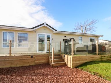 An exterior view of a single-story house with a wooden deck and glass railing at A and C Lodge-Plot 21 in Armathwaite