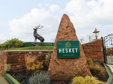 A stone sign with the text Hesket Caravan Park next to a deer statue and a brick wall at A and C Lodge-Plot 21 in Armathwaite