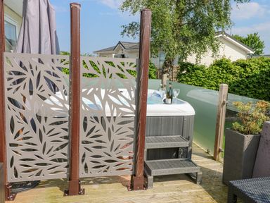 An outdoor deck area with a hot tub bottle and glasses on the edge decorative privacy panels wooden steps and plants at A and C Lodge-Plot 21 in Armathwaite