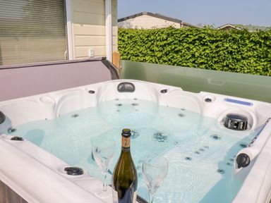 An outdoor hot tub with water and two empty wine glasses and a wine bottle at A and C Lodge-Plot 21 in Armathwaite