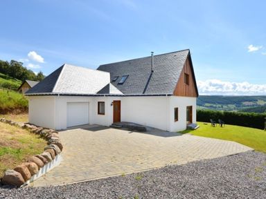 A house with a paved driveway and grassy lawn with chairs at Glen View Lodge in Drumnadrochit Loch Ness