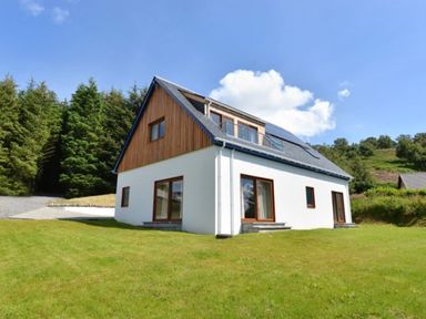 A two-story house with white walls and wooden accents surrounded by green lawn and trees at Glen View Lodge in Drumnadrochit Loch Ness