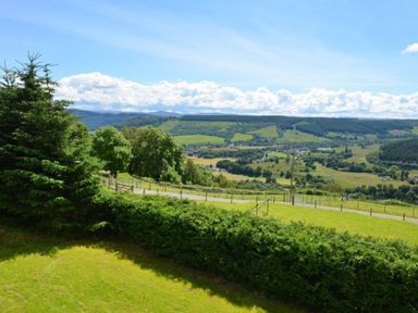 A grassy landscape with trees and hills under a blue sky at Glen View Lodge in Drumnadrochit Loch Ness