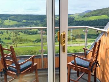 A balcony with two wooden chairs facing a green valley at Glen View Lodge in Drumnadrochit Loch Ness