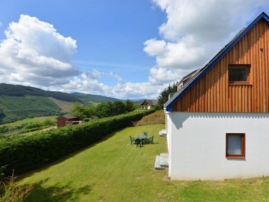 A side view of a house with a garden table and chairs on a grassy lawn with hills in the background at Glen View Lodge in Drumnadrochit Loch Ness