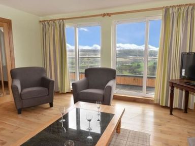 A living room with two armchairs a coffee table with glasses and large windows with curtains at Glen View Lodge in Drumnadrochit Loch Ness