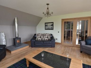 A living room with a leather sofa a wood stove a wooden coffee table and glass doors at Glen View Lodge in Drumnadrochit Loch Ness