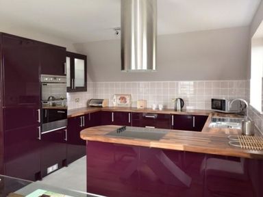 A kitchen with burgundy cabinets wooden countertops a built in oven a stainless steel cooker hood and a microwave at Glen View Lodge in Drumnadrochit Loch Ness