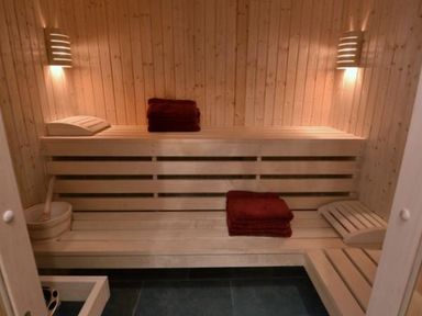 An indoor sauna with wooden bench seating lights towels and a wooden bucket with ladle at Glen View Lodge in Drumnadrochit Loch Ness