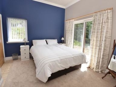 A bedroom with a double bed between two nightstands with lamps and large windows with curtains at Glen View Lodge in Drumnadrochit Loch Ness