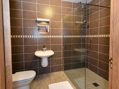 A bathroom with a toilet sink round mirror and walk in shower with glass partition at Glen View Lodge in Drumnadrochit Loch Ness