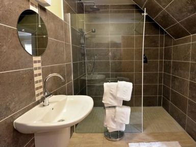 A bathroom with a wall-mounted sink mirror and a walk-in shower with folded towels at Glen View Lodge in Drumnadrochit Loch Ness