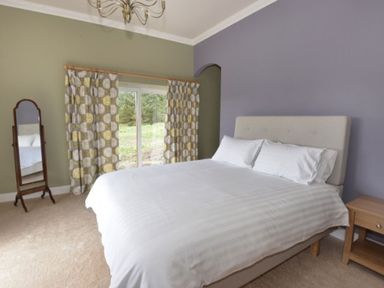 A bedroom with a bed a side table a standing mirror and curtains at Glen View Lodge in Drumnadrochit Loch Ness