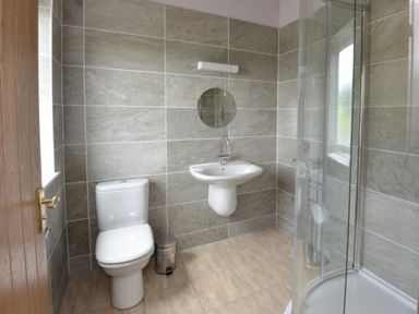 A bathroom with a toilet sink round mirror and glass shower at Glen View Lodge in Drumnadrochit Loch Ness