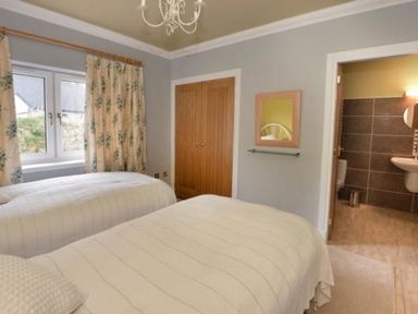 A bedroom with two single beds, floral curtains, a wooden wardrobe, a mirror on the wall and an open door leading to a bathroom at Glen View Lodge in Drumnadrochit Loch Ness