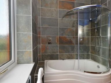 A bathroom with a bathtub shower combination and a window at Glen View Lodge in Drumnadrochit Loch Ness