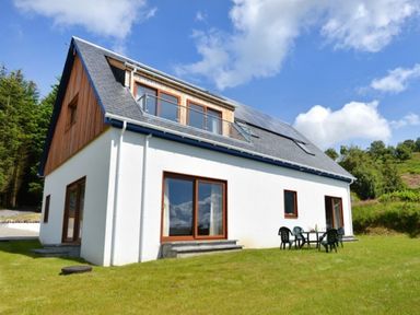 A modern house with white walls and wood paneling with patio doors and a table with chairs on grass at Glen View Lodge in Drumnadrochit Loch Ness