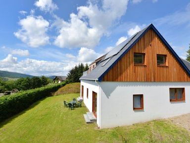 A house with a wooden upper floor and white lower floor on a grassy lawn with outdoor chairs and a table at Glen View Lodge in Drumnadrochit Loch Ness