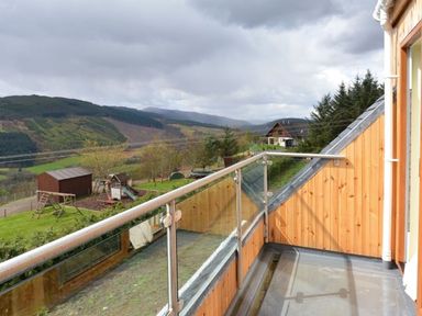 A balcony with glass railing overlooking a grassy area with playground equipment and hills in the background at Glen View Lodge in Drumnadrochit Loch Ness