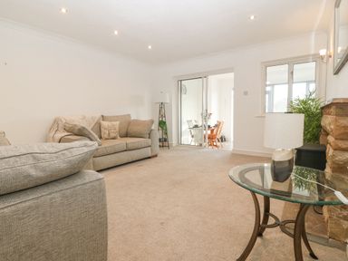 A living room with beige sofas a floor lamp a glass side table with a lamp and a stone fireplace at Riverview Apartment in Cemaes Bay