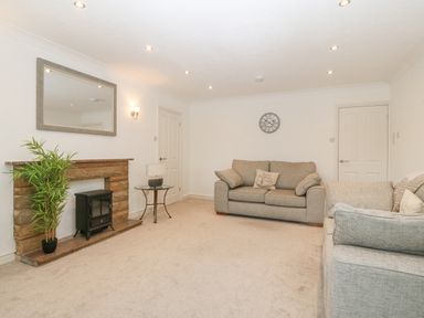 A living room with two sofas a round glass side table a clock on the wall a mirror above a fireplace with a potted plant next to it at Riverview Apartment in Cemaes Bay