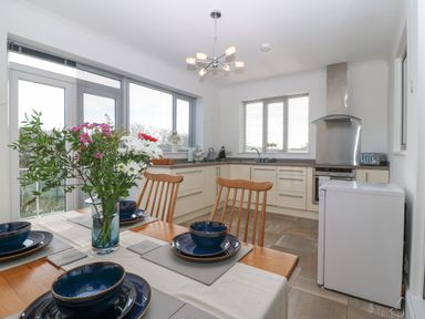 A kitchen with dining table set with blue dishes and flowers on the table at Riverview Apartment in Cemaes Bay