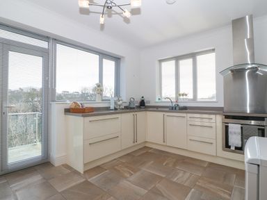 A kitchen with cream cabinets, stainless steel oven and hood, two windows with blinds and a glass door at Riverview Apartment in Cemaes Bay