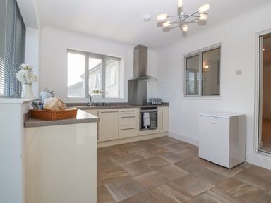 A kitchen with cabinets an oven a range hood a small fridge and a countertop with a basket and flowers at Riverview Apartment in Cemaes Bay