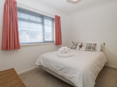 A bedroom with a bed white bedding three decorative pillows and folded towels near a window with pink curtains at Riverview Apartment in Cemaes Bay