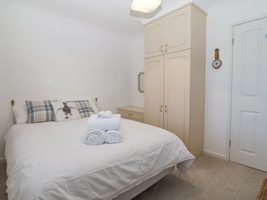 A bedroom with a bed with white bedding and pillows next to a cream wardrobe and drawer at Riverview Apartment in Cemaes Bay