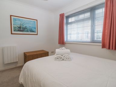 A bedroom with a bed and folded towels on it a window with blinds and curtains a wicker laundry basket and a framed painting on the wall at Riverview Apartment in Cemaes Bay