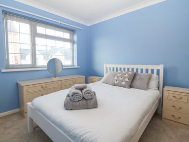 A bedroom with a white bed with pillows and towels on it beside beige dressers and a window at Riverview Apartment in Cemaes Bay