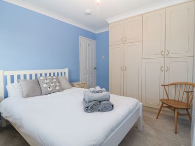 A bedroom with a white bed and folded towels on it a wooden chair a beige wardrobe and a nightstand at Riverview Apartment in Cemaes Bay