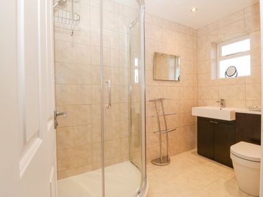 A bathroom with a glass shower enclosure a sink with cabinet a mirror towel rack and a toilet at Riverview Apartment in Cemaes Bay