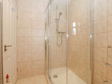 A bathroom with a glass shower enclosure and tiled walls at Riverview Apartment in Cemaes Bay