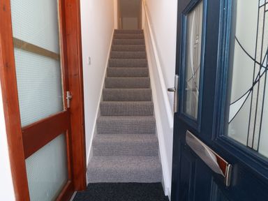 A narrow staircase with carpeted steps between a wooden door and a blue front door at Riverview Apartment in Cemaes Bay