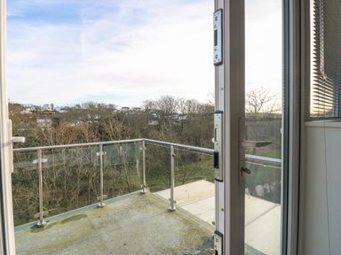 A balcony with glass and metal railings overlooking trees and houses at Riverview Apartment in Cemaes Bay