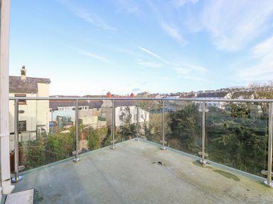 A balcony with glass and metal railing overlooking houses and trees at Riverview Apartment in Cemaes Bay