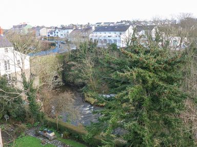 A river flowing through a residential area with houses trees and a stone bridge at Riverview Apartment in Cemaes Bay
