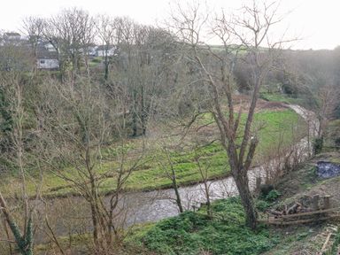 A river flowing through a grassy and wooded area with houses on the hill at Riverview Apartment in Cemaes Bay
