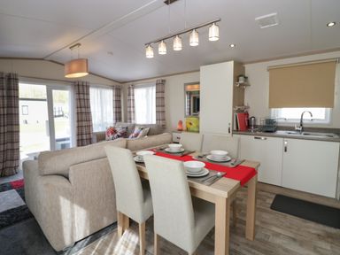 A living and dining area with sofas and a dining table set for four beside a kitchen at Ladybird Lodge South Lakes Leisure Park near Carnforth