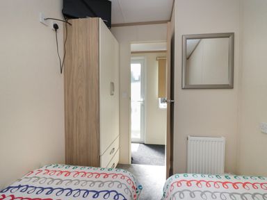 A bedroom with two single beds a wardrobe a wall-mounted TV a mirror and a door leading to another room at Ladybird Lodge in South Lakes Leisure Park near Carnforth