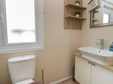 A bathroom with a toilet next to a frosted window and a sink with a mirror and shelves above at Ladybird Lodge South Lakes Leisure Park near Carnforth