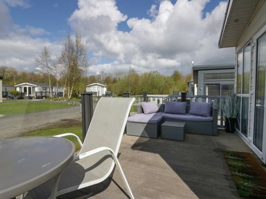 An outdoor patio with a glass table and chair and a cushioned wicker sofa set at Ladybird Lodge South Lakes Leisure Park near Carnforth