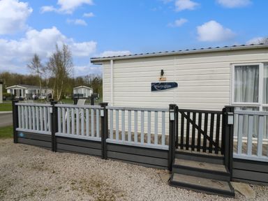 A white and grey mobile home with a small deck and gate on a gravel area at Ladybird Lodge South Lakes Leisure Park near Carnforth