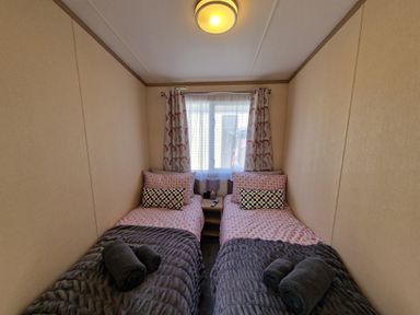 A bedroom with two single beds and a window with curtains at Ladybird Lodge South Lakes Leisure Park near Carnforth