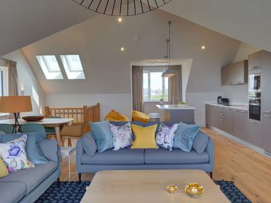An open plan living room and kitchen with blue sofas and colorful cushions at Villa 1 in Mullion