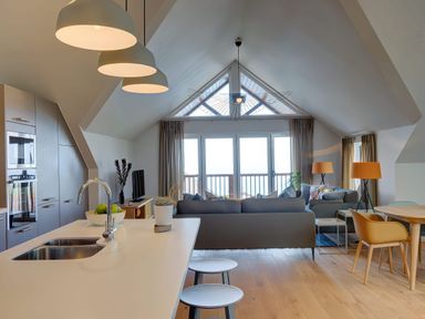 An open-plan living area with a kitchen island and stools a dining table with chairs sofas and large windows at Villa 1 in Mullion
