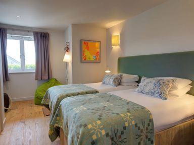 A bedroom with two beds side by side a green bean bag near the window and wall decorations at Villa 1 in Mullion