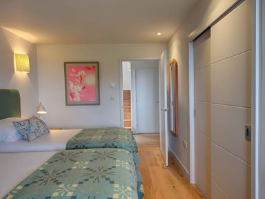 A bedroom with two beds with green patterned bedspreads a bedside table and lamp a framed picture on the wall a full length mirror a doorway and built in wardrobes at Villa 1 in Mullion